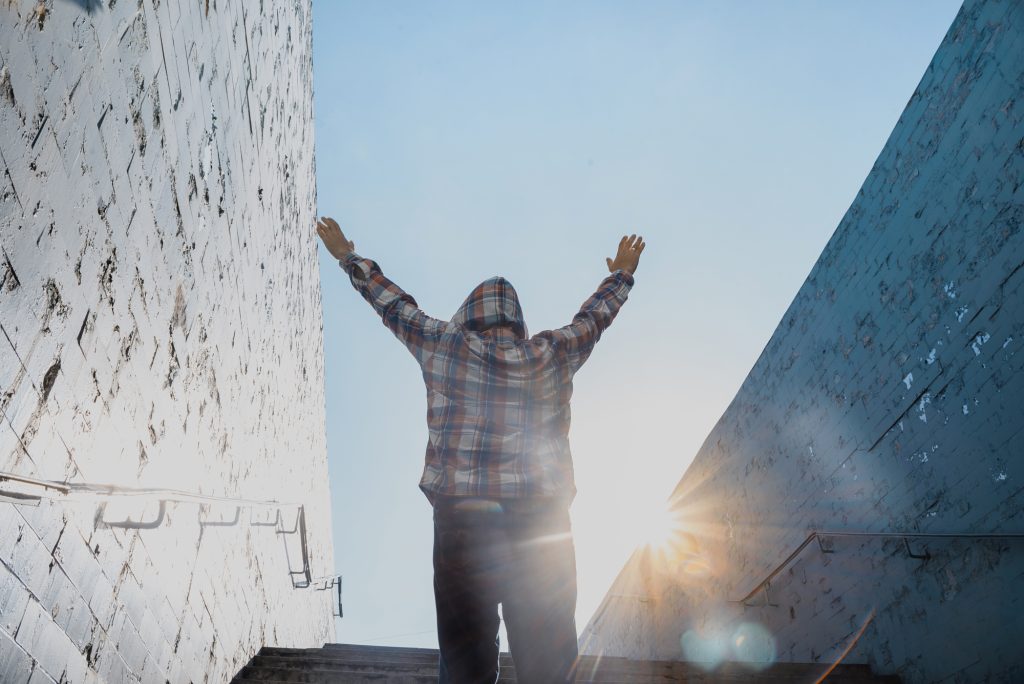 A person stands between two high walls with both arms raised toward the sunlight.