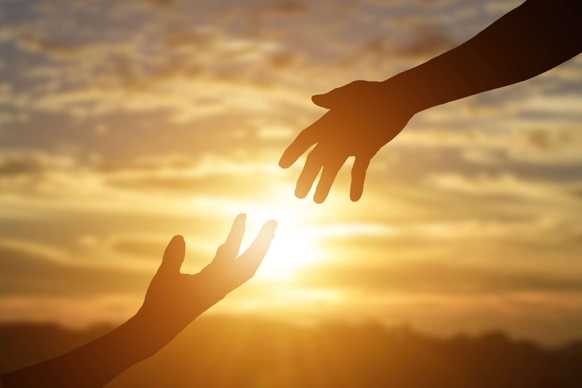 Two hands reach toward each other in silhouette against a golden sunset sky.